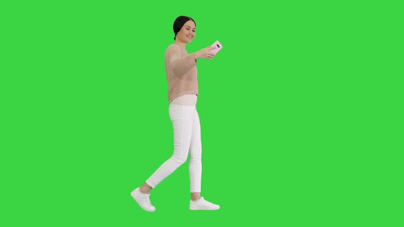 Pretty Smiling Female in Casual Clothes Taking Selfie While Walking on a Green Screen, Chroma Key.