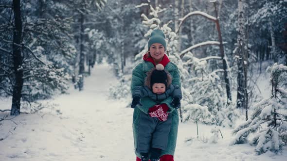 Young Happy Mother Having Fun and Playing with Toddler Son in Snowy Forest in Winter