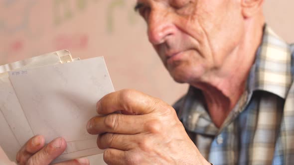 Portrait of a pensive caucasian pensioner 70 years old looking at old photos holding in his hands.Sl