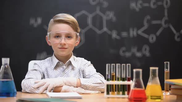 Little Genius Sitting in Protective Glasses, Chemical Liquids in Tubes on Table