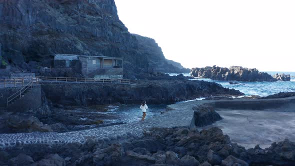 Aerial tracking shot girl running on promenade between lava and ocean