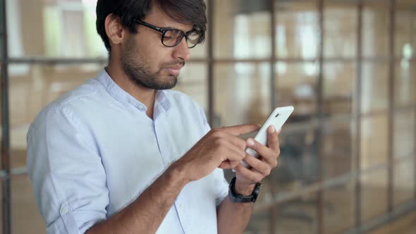 Young Indian Business Man Using Cellphone Apps Standing in Office