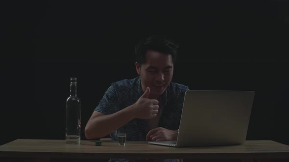 Drunk, Smiling Asian Man Drinking Vodka During Having Video Call On A Laptop In Black Background