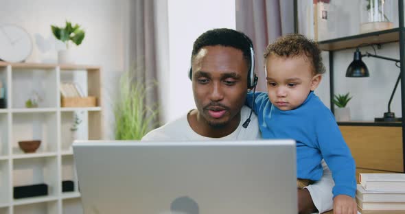 Man which Caring About His Little Son at Home and Talking on Computer with Friends or Relatives