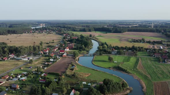 Aerial rural shot of a curvy river with a wooden bridge, running by a small farming village. Lake vi