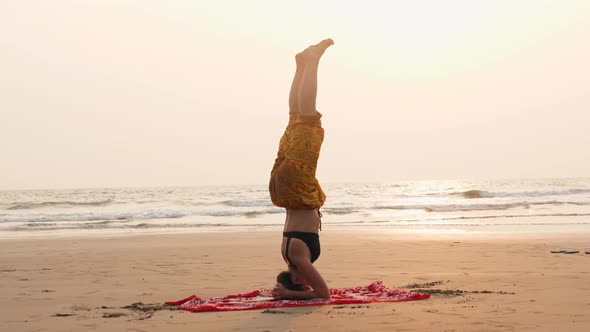 Serenity and Yoga practicingIs on the Head Woman Near Ocean Doing Headstand Upside Down