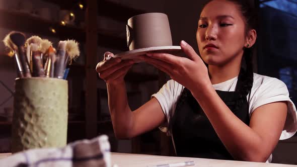 Pottery in the Art Studio Asian Woman Takes a Plate with a Clay Cup on It and Looking at It Brushes