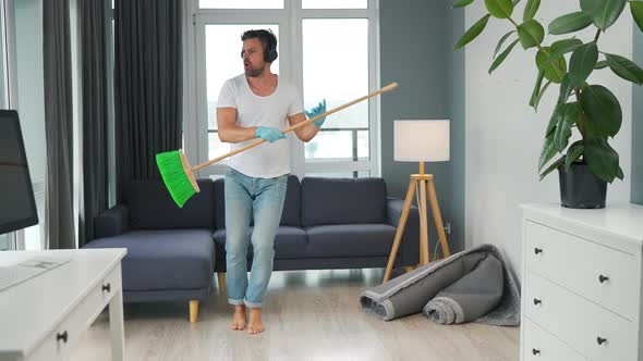 Man in Headphones Does the Cleaning and Imagines Himself a Rock Star Plays the Broom Like a Guitar