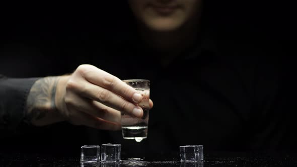 Barman Pour Frozen Vodka From a Bottle Into a Glass with Ice. Black Background