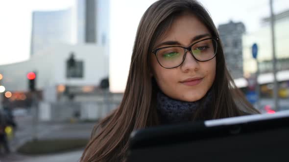 Beautiful young woman using tablet outdoor in the evening with face illuminated by screenlight