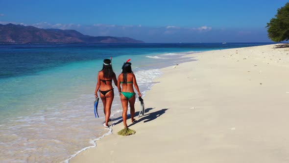 Pretty happy ladies on photoshoot by the sea on beach on sunny blue and white sand background 4K