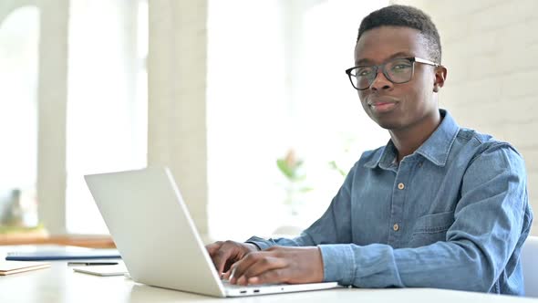 Young African Man with Laptop Pointing with Finger at Camera