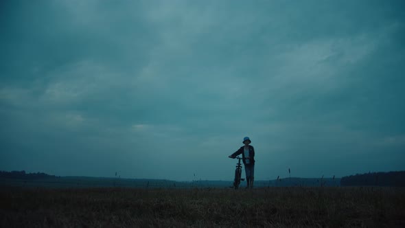 Boy With A Bicycle Walking In A Field In Rainy Weather at the Top of the Field Goes Into the