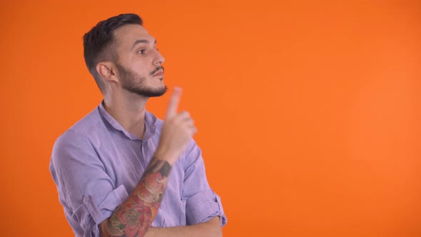 Thoughtful Man Looking Up with Finger on Face or Chin, Isolated on Orange Background.