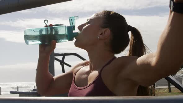 Sporty Caucasian woman drinking water in an outdoor gym during daytime