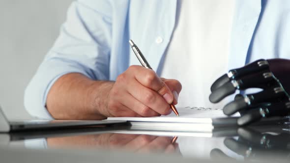 Skilled employee man with artificial high tech limb writes orders in paper notebook