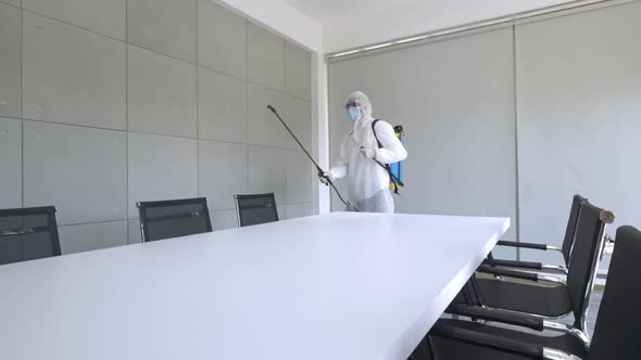 Worker in PPE suit cleaning in building with spray disinfectant water to remove covid 19