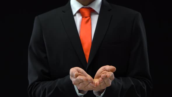 Man in Black Suit Opens Palms While Holding Something in His Hands at Black Background. Mockup Ready