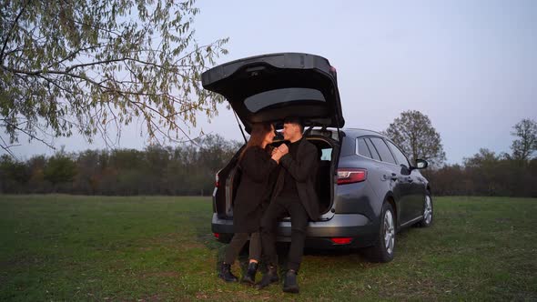 Happy Loving Couple of Travelers Stand Next to Car and Admire Beautiful Sunset