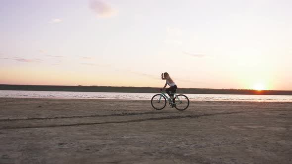 Young Attractive Woman Riding Biycle on the Beach Near the Sea During Sunrise or Sunset Slow Motion