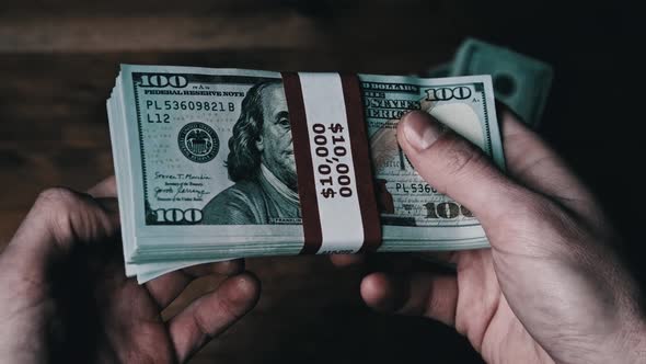 Stack of 10000 American Dollars Banknotes in Male Hands Over Wooden Background