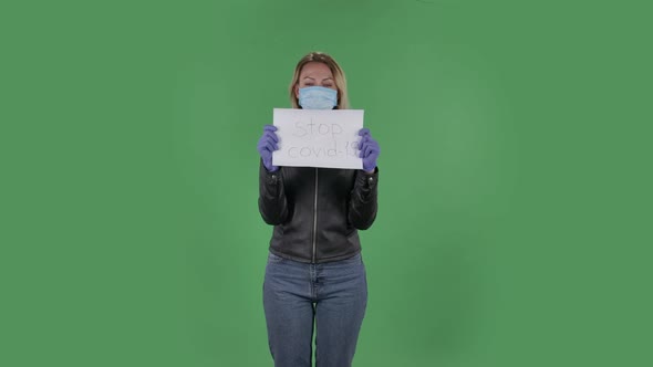 Portrait of Beautiful Young Woman in Medical Mask Is Looking at Camera and Holding a Poster Stop