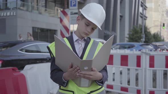 Portrait Little Boy Wearing Safety Equipment and Constructor Helmet Reading Building Plan