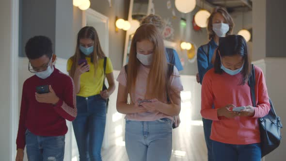 Group of Multiethnic Children in Safety Mask Walking Along School Corridor and Using Smartphone