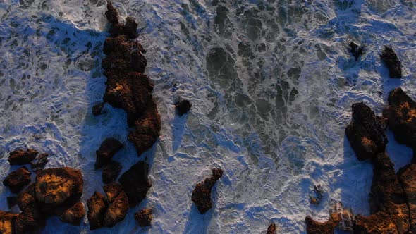 Spectacular top down aerial drone view of rough waves crashing the rock shore