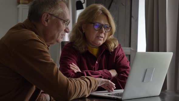 two elderly people surfing internet on laptop computer at home.