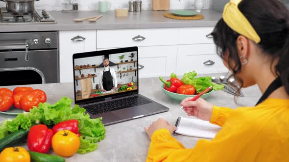 Woman in Kitchen Study Online Video Call Laptop Greets Chef Writes in Notebook