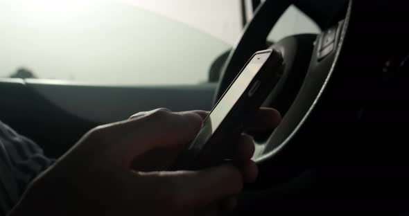 Man typing in smartphone while sitting in car, close up.