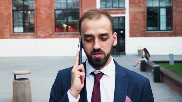 Businessman in Suit Walking and Talking on the Phone in Front of the Business District