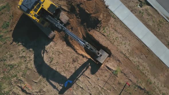 A drone pull away and spin creating a bird’s eye view of a backhoe excavator beginning to dig a hole