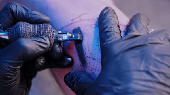 A Session in Tattoo Salon  Filling in the Tattoo with Black Color Under the Blue Light