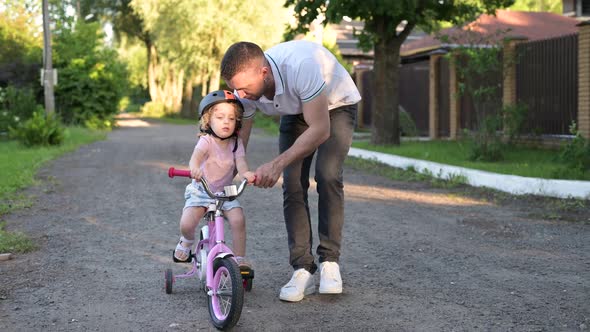 Father teaches little daughter to ride a bike. Little girl wearing a helmet