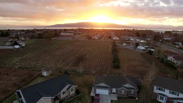 Aerial view of sunset above Orem Utah moving towards Utah Lake passing homes and field.