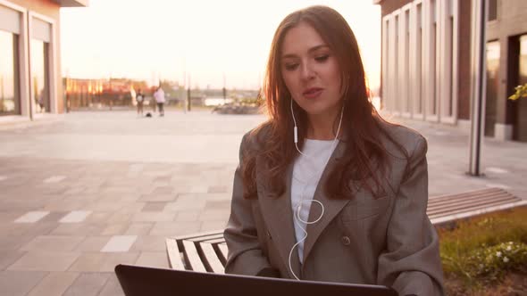 Young attractive business woman sitting outdoor on the bench using laptop