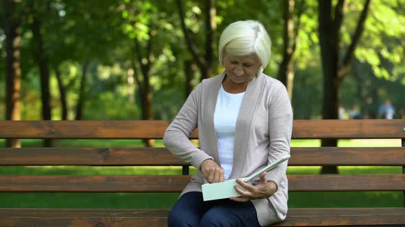 Old Lady Sitting on Bench Looking at Pendant, Remembering Her Husband, Loss