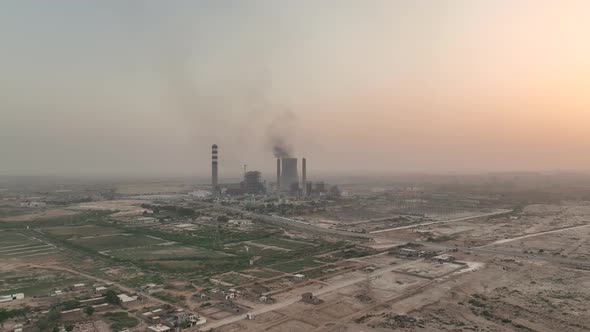 Cinematic aerial shot of silver car driving on country road in desert and big chimneys in distant ba