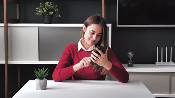 Smiling Young Business Woman Reading News on Phone Makes Online a Purchase Sit at Home Office Desk