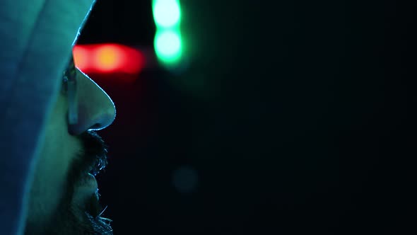 Matrix style bearded man sidewas, face almost covered by hood. Green and red led lights background.