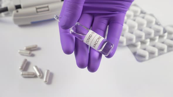 Ampoule with a vaccine against coronavirus in a hand in a surgical glove 