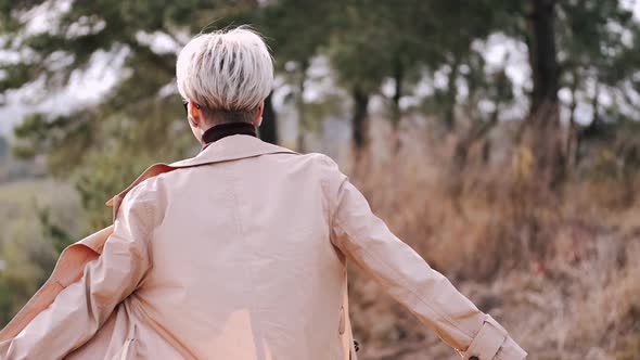 Portrait of Young Stylish Woman in Coat Dancing in Forest