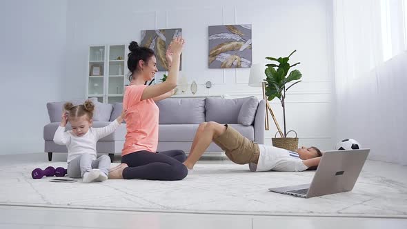 Mother Exercises with Ball Together with Her Son and Her Cute Small Daughter Interfering Her