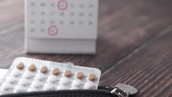 Birth Control Pills and Calendar on Wooden Background Close Up