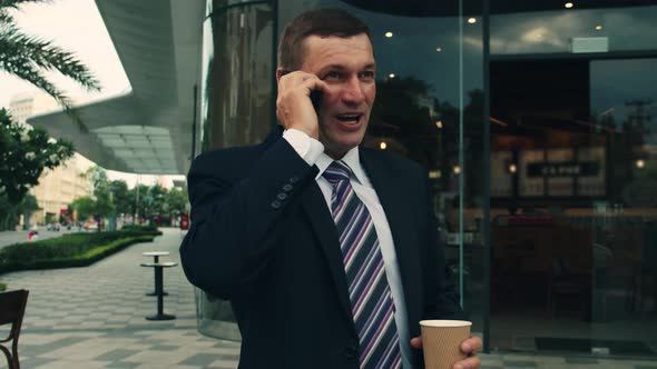 The Shot Moves Around a Businessman Standing on Street in the City Center Who Uses the Phone for