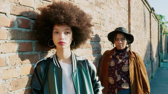 Two cool hipster friends leaning on brick wall