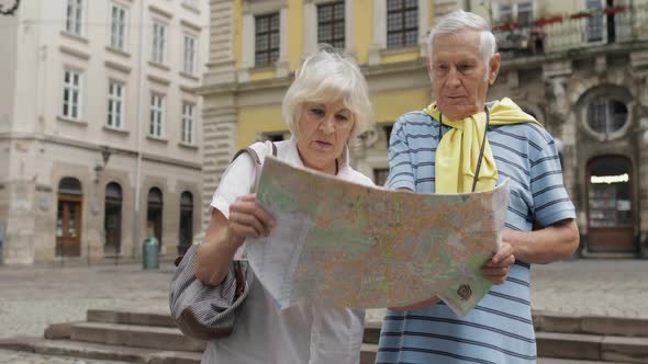 Senior Male and Female Tourists Walking with a Map in Hands Looking for Route
