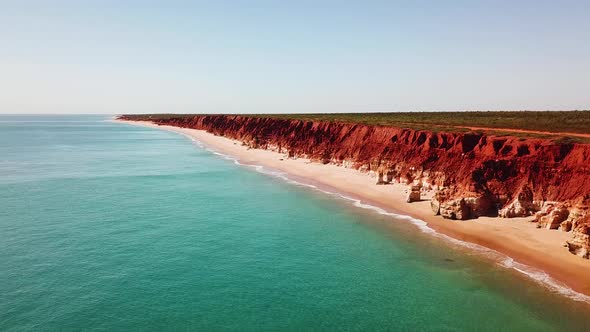 Drone flying adjacent to spectacular red ocean side cliffs and blue water of Western Australia